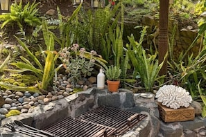 A garden with various plants, a grill, and a decorative white object.