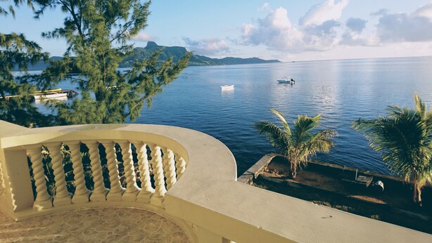 Un balcon donnant sur une mer calme, un petit bateau et des montagnes lointaines.