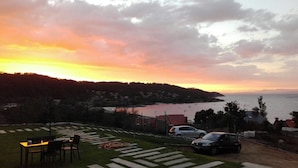 Una terraza con asientos al aire libre, vista al mar y coches aparcados.