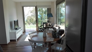 Un comedor moderno con una mesa de madera, sillas blancas, un jarrón con follaje y un portátil sobre una consola blanca.