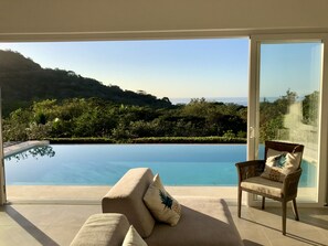 A room with a large glass door leading to a pool and a view of the sea.