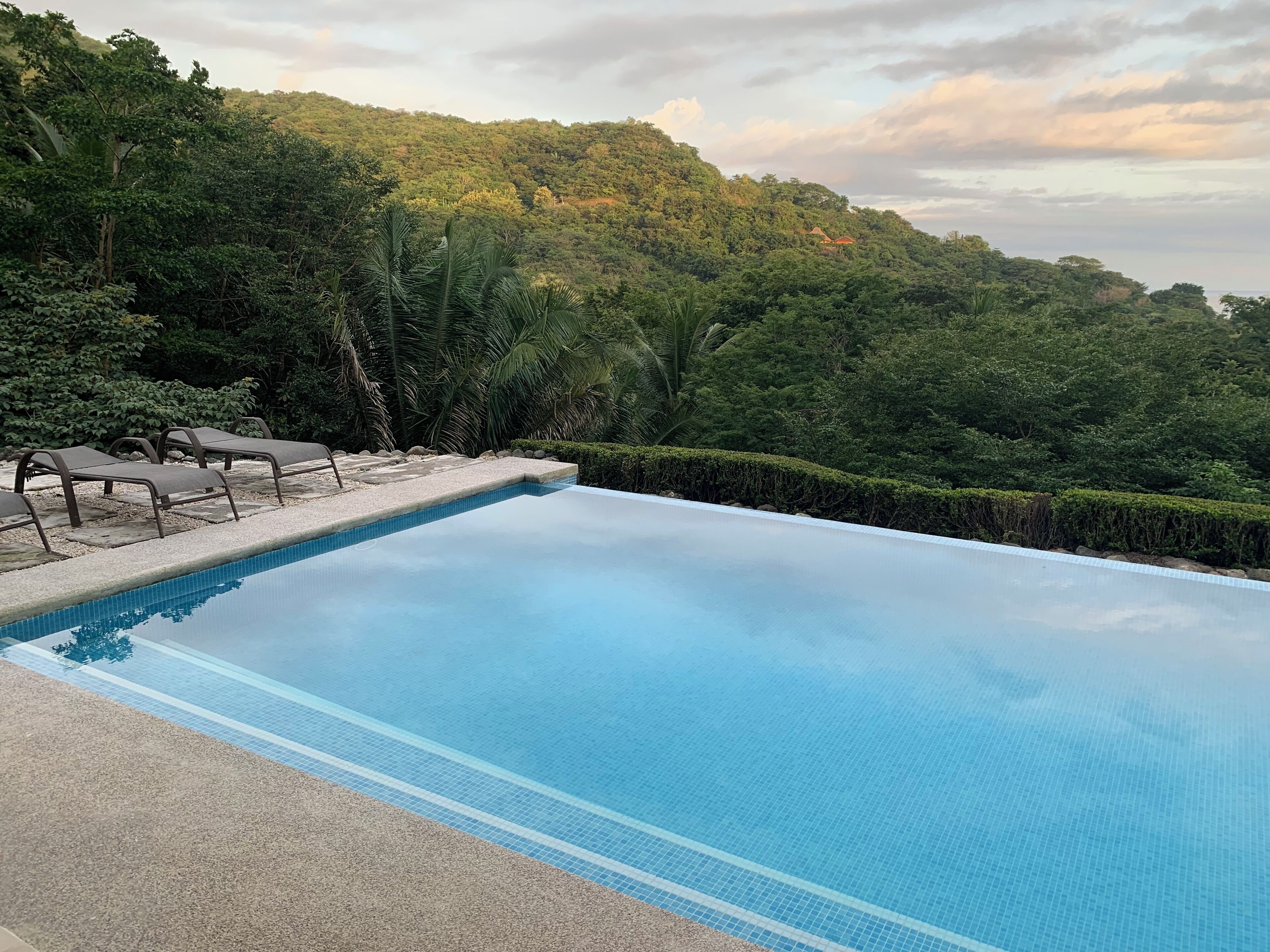 A rectangular pool with clear blue water, surrounded by a pebble-lined deck and lounge chairs.