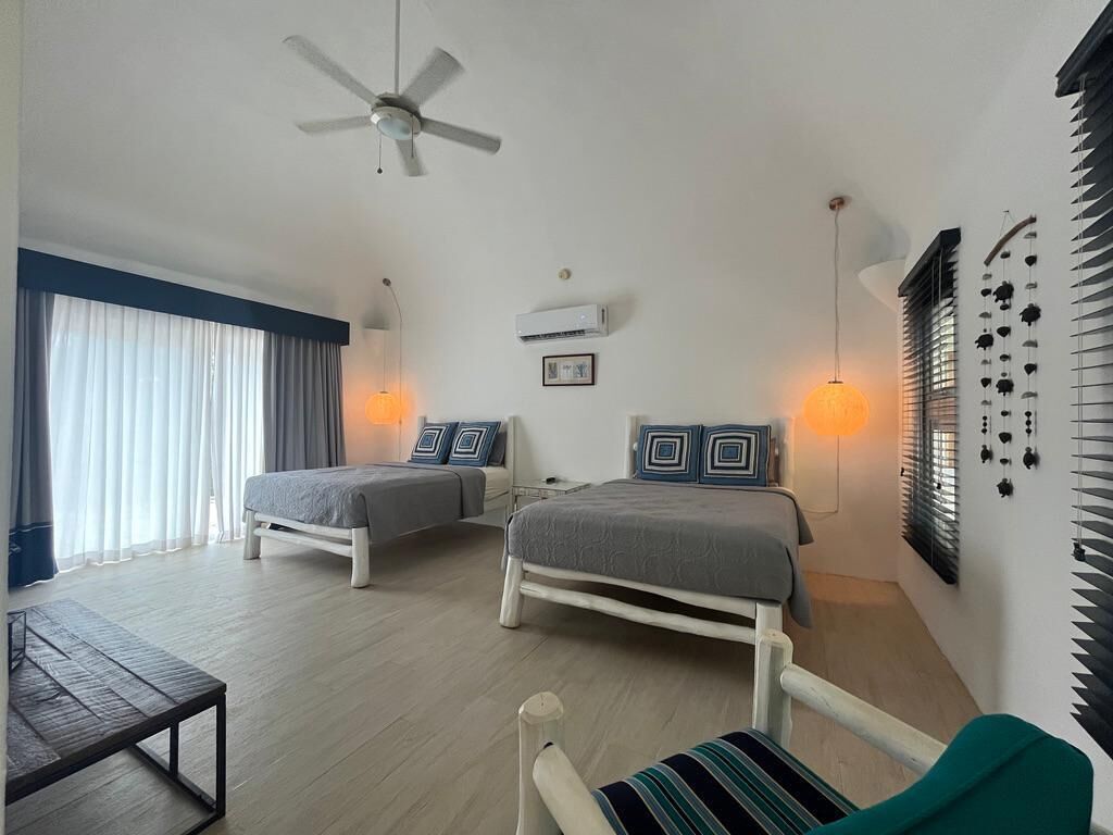 A bedroom with two beds, a ceiling fan, an air conditioner, and a bedside table.
