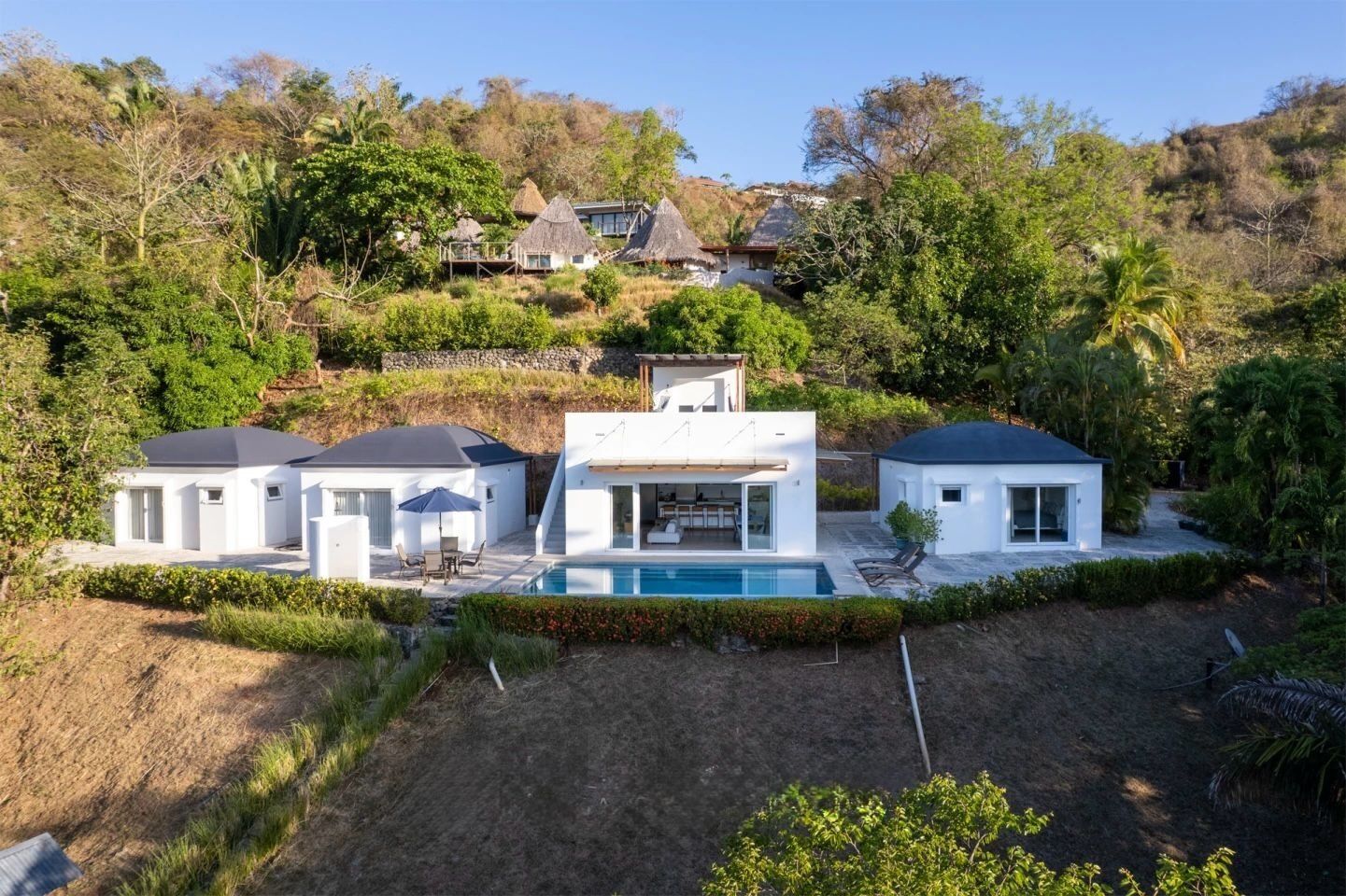 Ein modernes Haus mit Schwimmbad, umgeben von üppiger Vegetation und Hügeln.