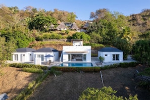 Una casa moderna con piscina, rodeada de exuberante vegetación y colinas.
