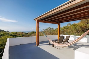 Una hamaca debajo de una pérgola de madera en una terraza en la azotea, con vista al océano.
