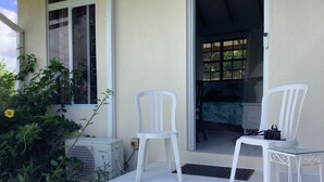 A white outdoor seating area with two chairs and a table, an air conditioning unit, and a window with a view of the interior. - Garden Delight Studio is conveniently located in Rodney Bay! (Rodney Bay)