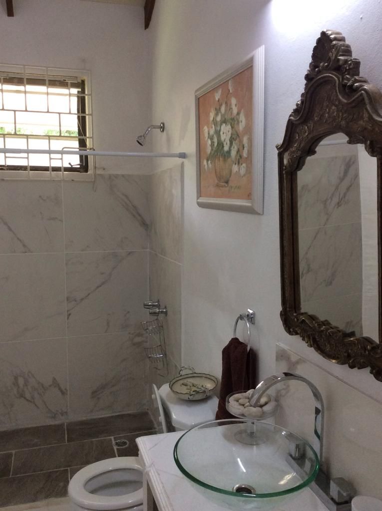 Un baño con lavabo de cristal, inodoro, ducha y un espejo decorativo.