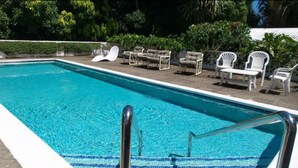 A rectangular swimming pool with clear blue water, surrounded by a paved deck. There are several white lounge chairs and a few tables with chairs on the deck. - Garden Delight Studio is conveniently located in Rodney Bay! (Rodney Bay)