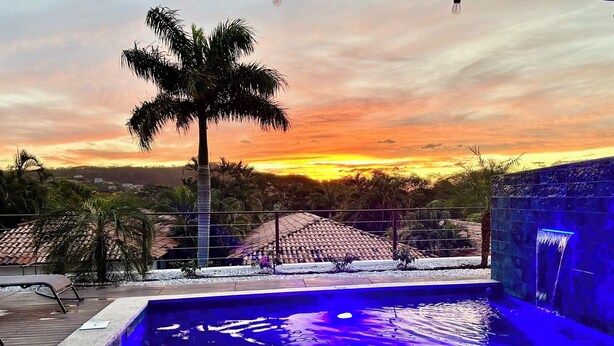 A swimming pool with a sunset view, a palm tree, and a tiled roof structure.
