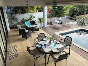 A covered outdoor area with a pool, seating, and potted plants.