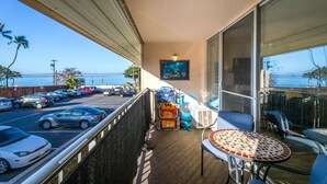 A balcony with a view of the ocean, a table, chairs, and luggage.