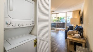 A laundry area with a washing machine, a closed louvered door, and a view of a balcony with outdoor furniture.