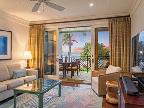 Ein Hotelzimmer mit einer Couch, einem Glastisch, einem Sessel, einem kleinen Tisch mit einer Lampe, einem Fernseher und Blick auf den Ozean.