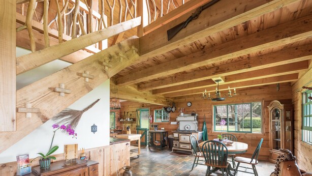 A rustic wooden interior with exposed beams, a dining area with a round table and chairs, and a kitchen with wooden cabinets and a stove. - Until you experience it you don't know it exist... Exceeded Expectations (Hawi)