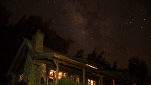 A stone house with a covered porch and lit windows, surrounded by a grassy lawn and trees. - Until you experience it you don't know it exist... Exceeded Expectations (Hawi)