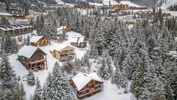 Ein schneebedecktes Bergresort mit mehreren Holzbauten, darunter Blockhütten und Chalets, umgeben von dichten Nadelbäumen.