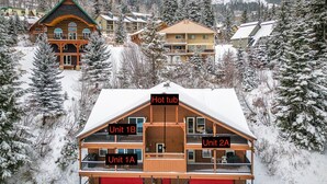 Ein mehrstöckiges Lodge mit Whirlpool, gekennzeichnet als Einheit 1B, sowie zwei weitere Einheiten, Einheit 1A und Einheit 2A, umgeben von schneebedeckten Bäumen und anderen Gebäuden.