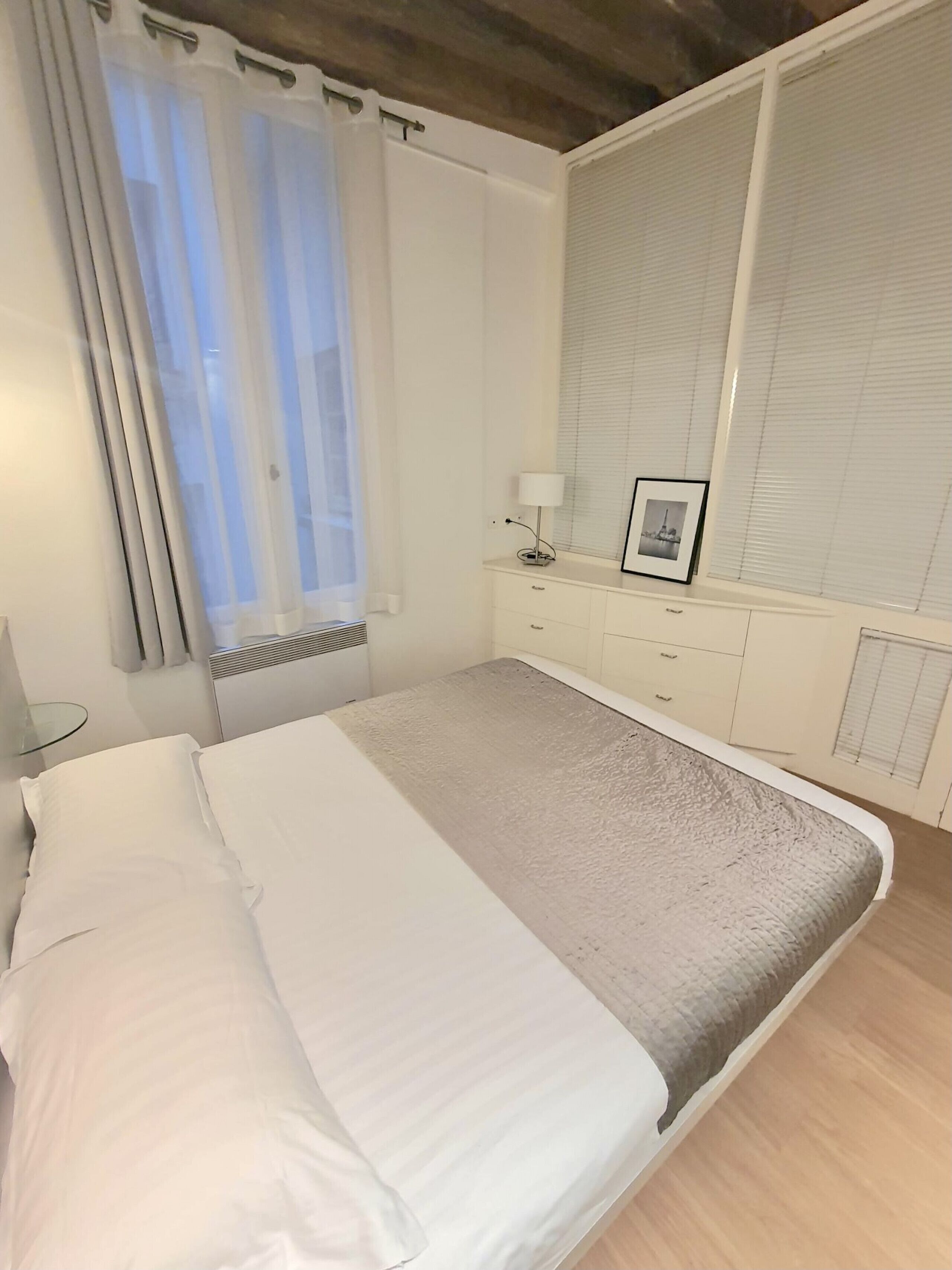 A bedroom with a bed, a bedside table, a lamp, and a window with blinds.