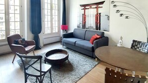Un salon avec un plafond en bois, un canapé gris, une table basse ronde, une petite table à manger et une chaise.