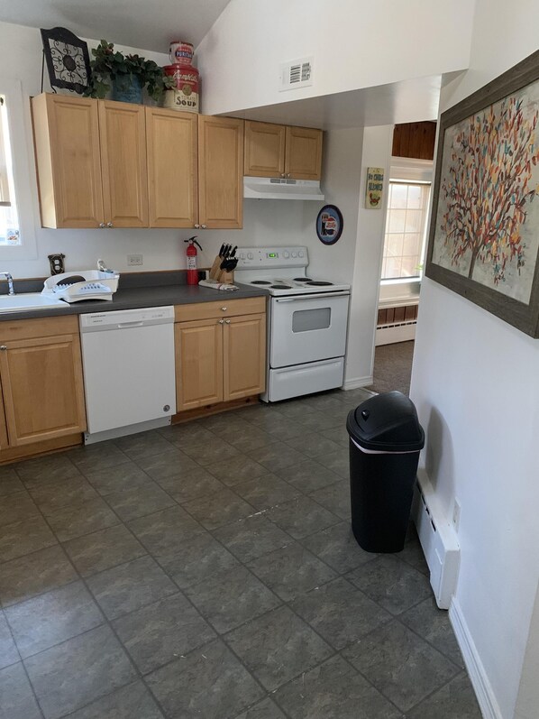 A kitchen with wooden cabinets, a white stove, a dishwasher, and a trash can. - Beautiful Spacious Escape On The Chain O'Lakes (Fox Lake)