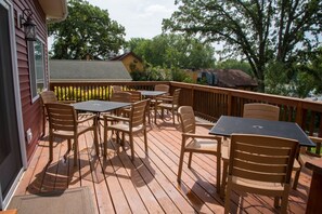 A wooden deck with outdoor furniture, including chairs and tables, overlooking a body of water and surrounded by trees. - Beautiful Spacious Escape On The Chain O'Lakes (Fox Lake)