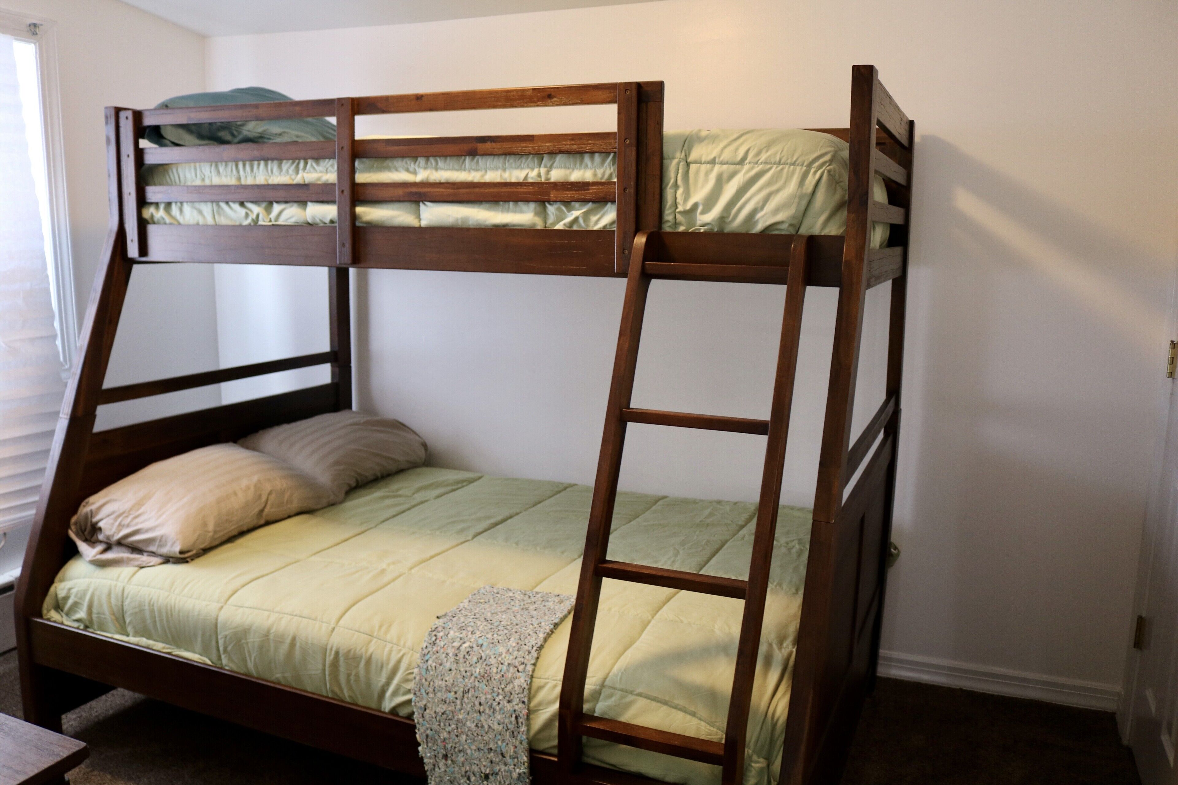 Una cama individual superpuesta con escalera, un edredón verde y una almohada.
