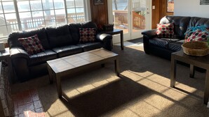 Una habitación acogedora con un sofá de cuero, una mesita de madera y una cesta de mimbre. Hay un cartel sobre la puerta que dice "Let's do Sunset".