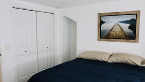 Un dormitorio con una colcha azul oscuro, un cuadro con un muelle de madera y puertas dobles blancas.