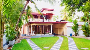 Set amidst lush greenery, this two-story house features a balcony and a garden with a lawn and potted plants.