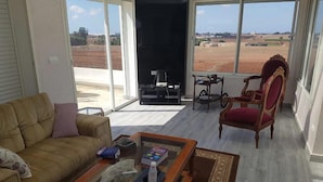 A living room with a sofa, a coffee table, and a chair. There is a fireplace and a view of a field through large windows.