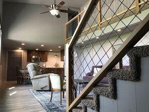 A modern kitchen with wooden cabinets, a dining area with a chair, and a staircase with a textured wall. - Surrounded by Salamonie State Park & Reservoir Newly Converted Barn! (Lagro)