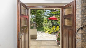 An open wooden door leading to a stone-tiled patio with yellow lounge chairs and a red umbrella.
