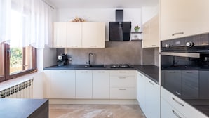 Une cuisine moderne avec des meubles blancs, une cuisinière noire et une fenêtre avec des rideaux.