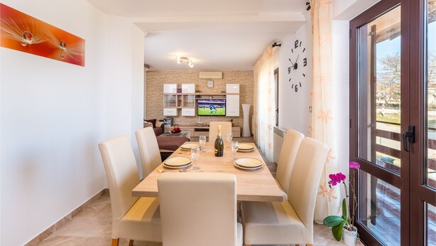 Un coin repas avec une table dressée pour quatre personnes, un téléviseur fixé au mur et une vue sur l’extérieur grâce à une grande fenêtre.