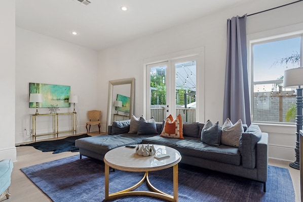 A modern living room with a grey sofa, a round coffee table, and a large window with curtains.
