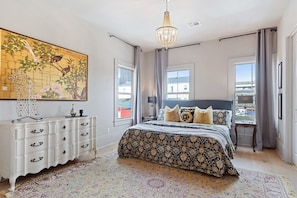 A bedroom with a large bed, a dresser, a chandelier, and a painting on the wall.
