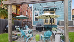 Un patio exterior con una parrilla, zona de estar y luces colgantes.