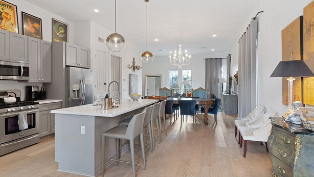 Una cocina moderna con electrodomésticos de acero inoxidable, una isla central con taburetes y un comedor con candelabro.