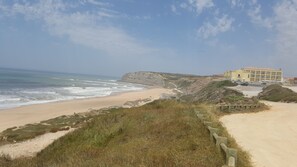 Un hotel frente al mar con playa de arena, acantilados rocosos y cielo despejado.