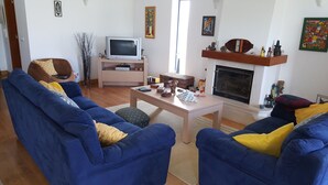 A living room with two blue sofas, a wooden coffee table, a television, a fireplace, and various decorative items. - Villa on Beach Azul Beach (Silveira)