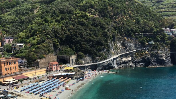Ein Küstenstrand mit klarem türkisblauem Wasser, einer Steinbrücke und einer Reihe von Strandsonnenschirmen.