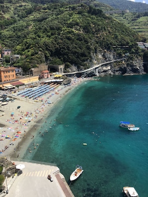 Una playa costera con aguas turquesas cristalinas, un puente de piedra y una hilera de sombrillas.