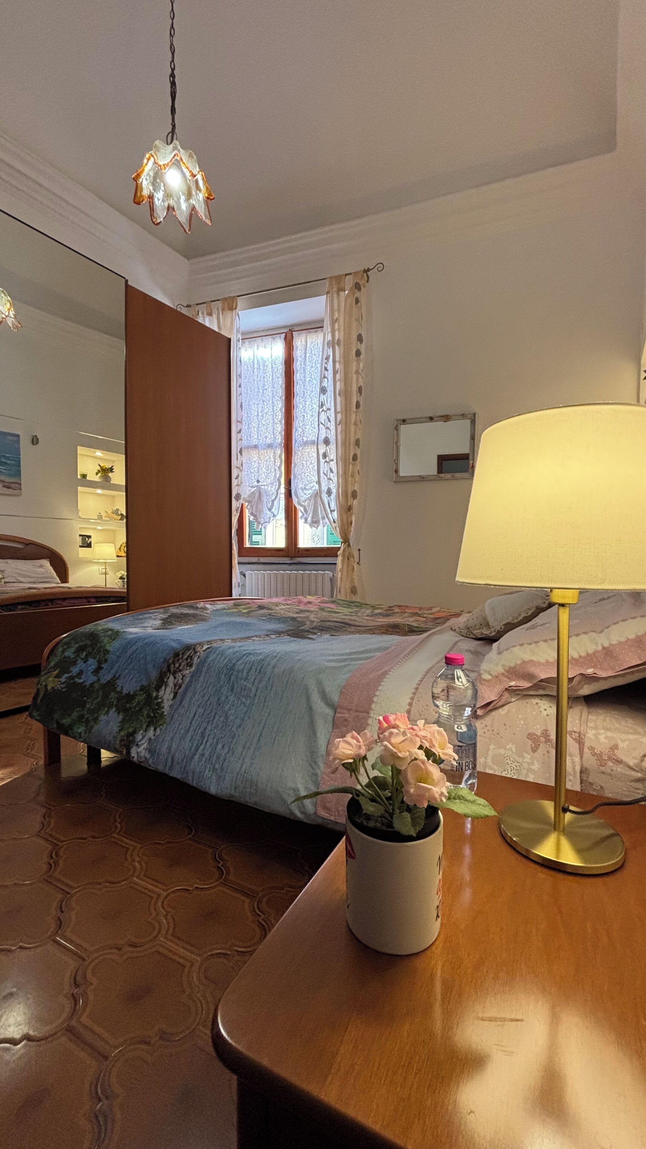 Ein Hotelzimmer mit Bett, Nachttisch mit Lampe, einem Fenster mit Vorhängen und Blick nach außen.