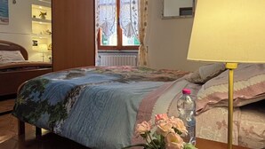 Ein Hotelzimmer mit Bett, Nachttisch mit Lampe, einem Fenster mit Vorhängen und Blick nach außen.