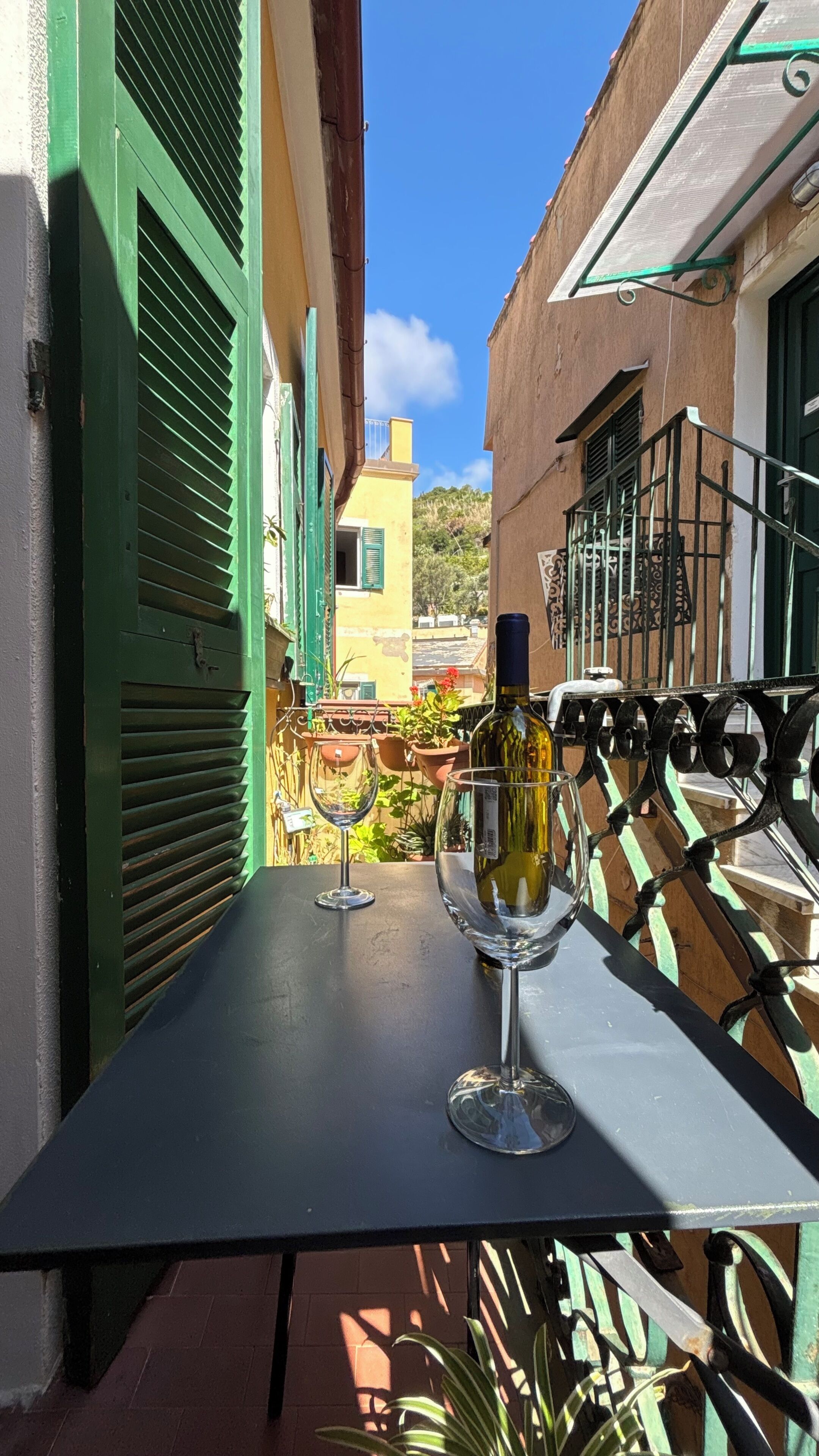 A balcony with a table, two wine glasses, and a bottle of wine.