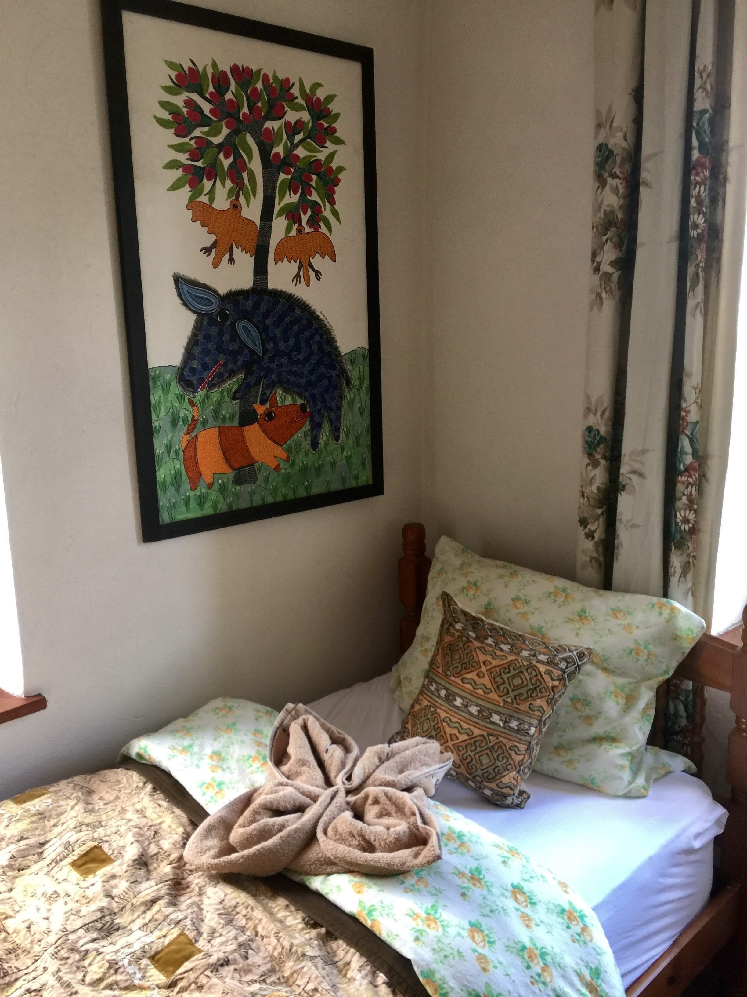Ein Schlafzimmer mit einem Bett, einem gerahmten Bild von Bäumen und Tieren, blumigen Vorhängen und einer gemusterten Tagesdecke.