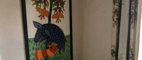 Ein Schlafzimmer mit einem Bett, einem gerahmten Bild von Bäumen und Tieren, blumigen Vorhängen und einer gemusterten Tagesdecke.