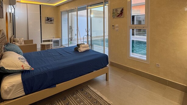 Un dormitorio moderno con una cama grande, vista al mar a través de una ventana e iluminación integrada en el techo.