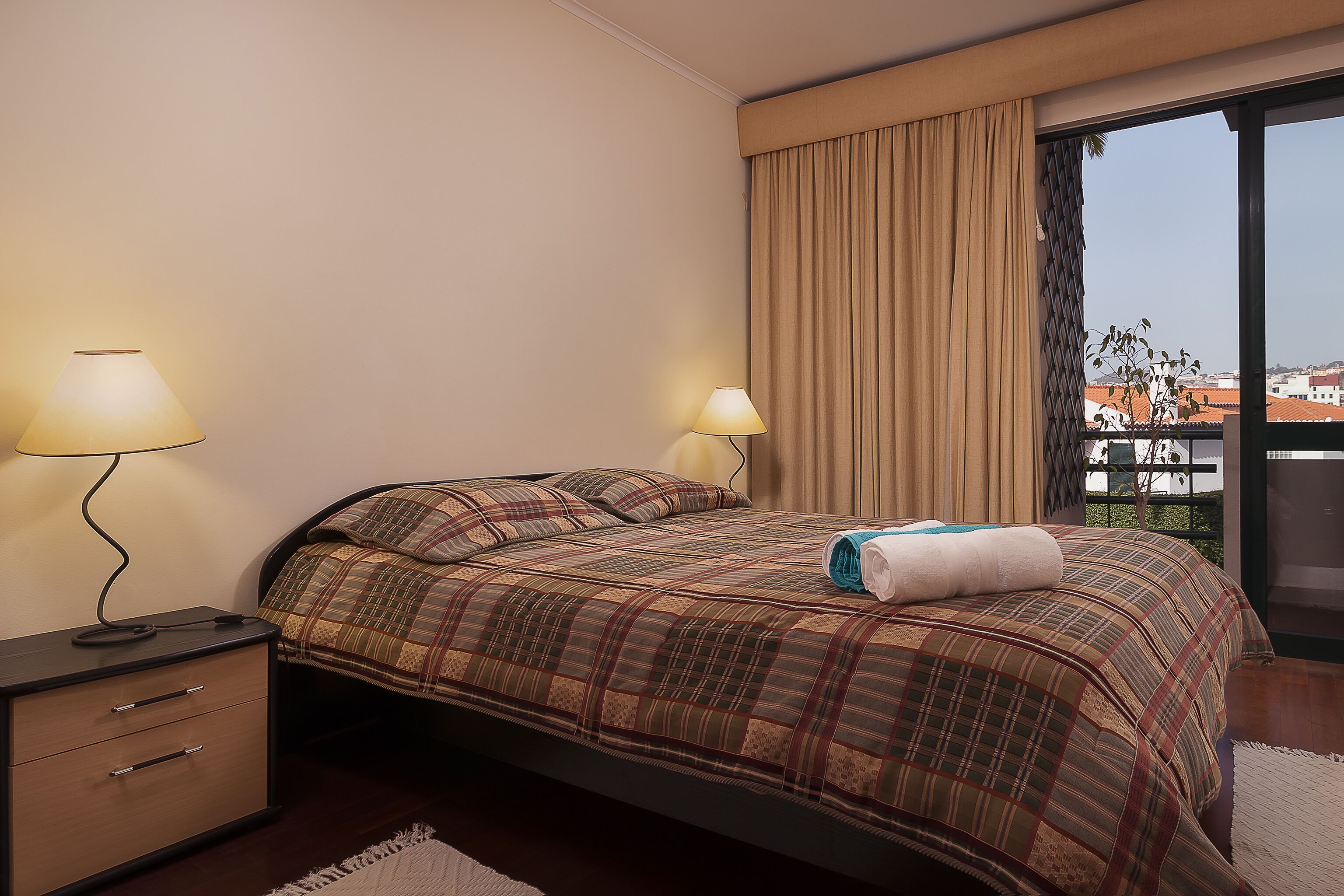 Une chambre à coucher avec un lit, deux lampes de chevet, une table de chevet et une vue sur l’extérieur grâce à une grande fenêtre.